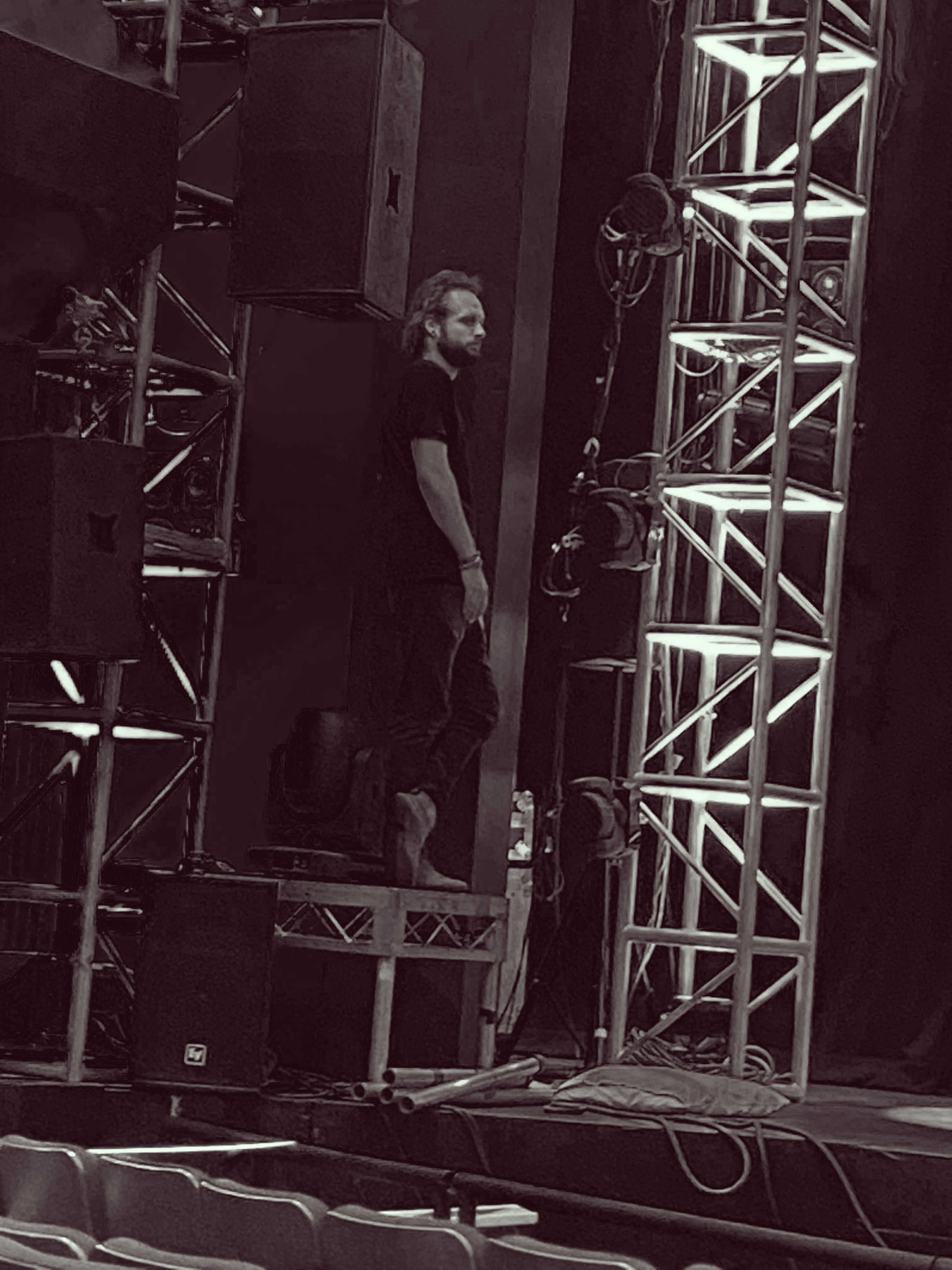 David Grigg backstage beside a PA stack and lighting truss.