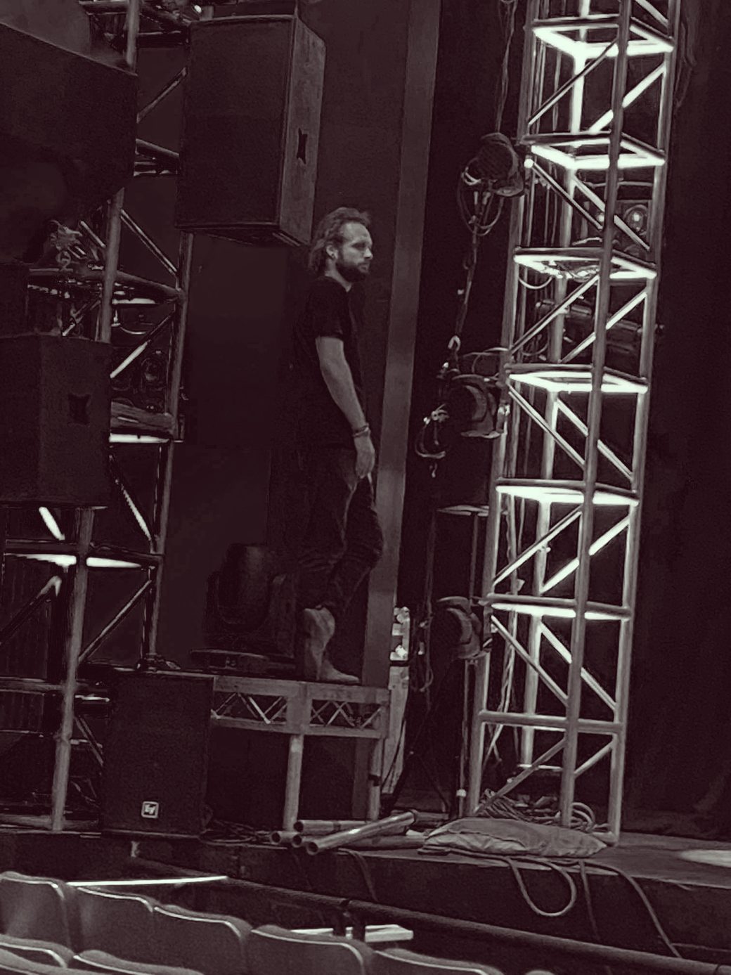 David Grigg backstage beside a PA stack and lighting truss.